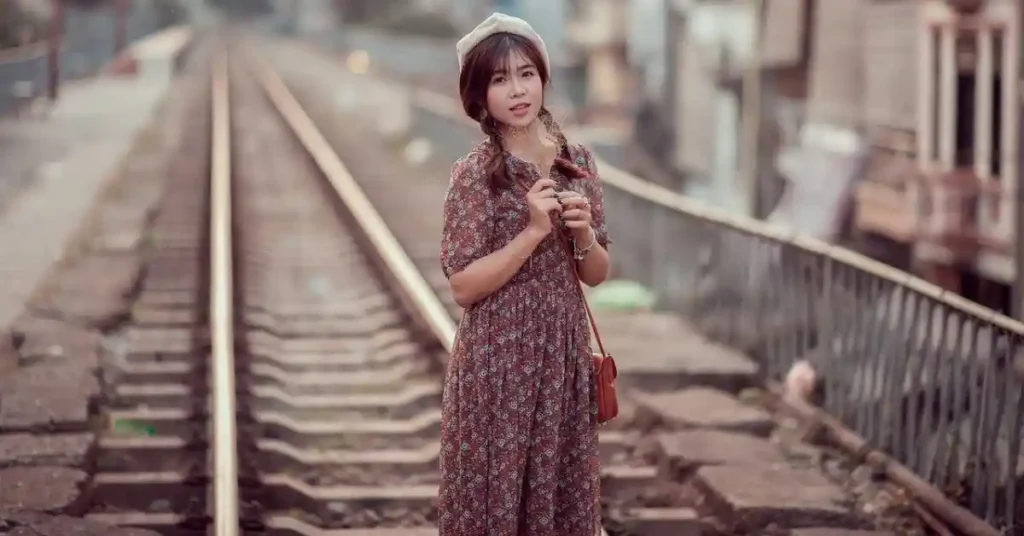 a beautiful girl is standing on an empty rail track, holding a flower in her hands, looking straight to the camera.